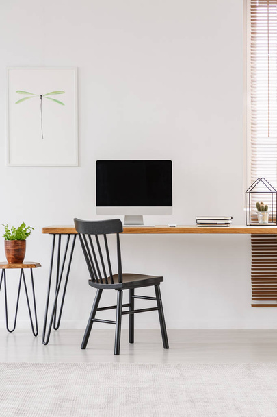 Simple interior of a home office with black chair standing at a wooden desk with an empty computer monitor. Real photo - 写真・画像