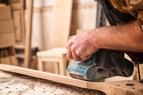 Молодий чоловік будівельник столяр дорівнює полірування дерев'яної дошки з випадковим шліфуванням орбіти в майстерні
 - Фото, зображення