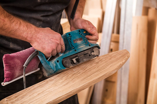Primer plano de un joven carpintero constructor es igual a pule tablero de madera con una lijadora de órbita aleatoria en el taller
 - Foto, Imagen