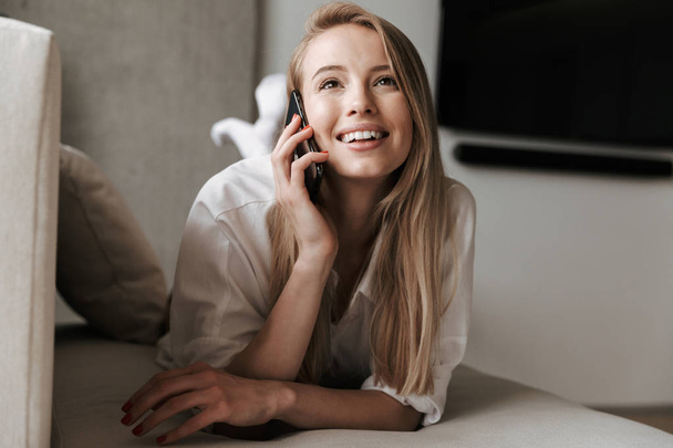Photo of smiling pretty young woman indoors at home talking by mobile phone. - Foto, Imagem
