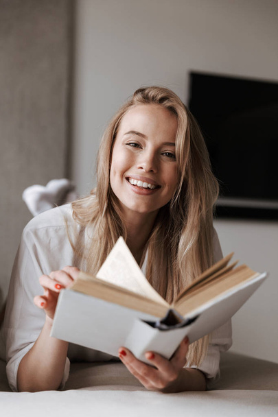 Smiling young woman holding blank cover open book while relaxing on a couch at home - Photo, Image