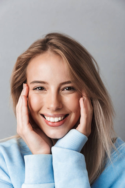 Close up of a happy young girl in blue sweatshirt looking at camera isolated over gray background - Foto, Imagem