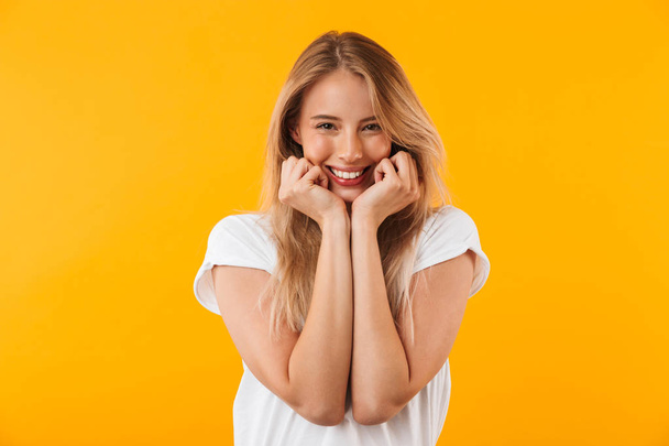 Portrait of a pretty young blonde girl looking at camera isolated over yellow background - Фото, изображение