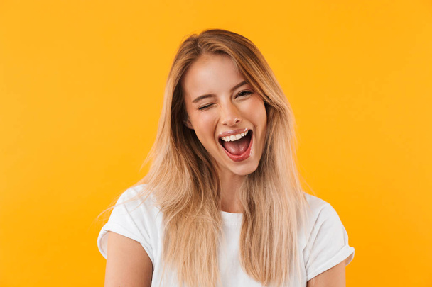 Portrait of a cheerful young blonde girl winking isolated over yellow background - Foto, imagen