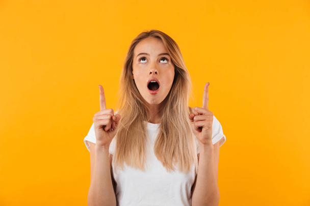 Portrait of a shocked young blonde girl pointing up at copy space isolated over yellow background - Фото, зображення