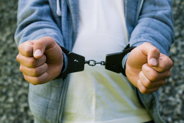 young criminal standing in handcuffs, outdoors. Concept of crime - Foto, afbeelding