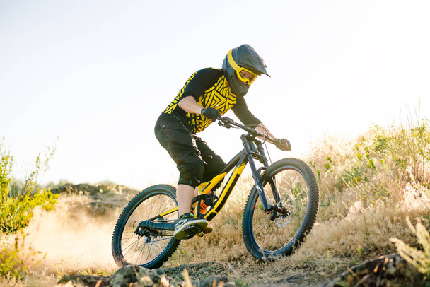 Professional Cyclist Riding the Downhill Mountain Bike on the Summer Rocky Trail at the Evening. Extreme Sport and Enduro Cycling Concept. - Foto, Imagem