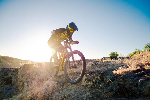 Ciclista profesional que monta la bicicleta de montaña cuesta abajo en el sendero rocoso de verano en la noche. Concepto de Ciclismo de Extremo Deporte y Enduro. - Foto, imagen