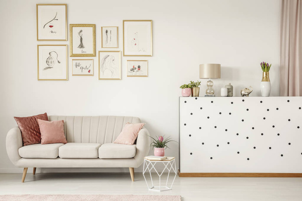 Pink pillow on beige sofa in feminine living room interior with plant and gallery of posters - Photo, image