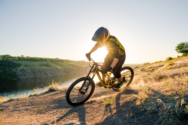 Professional Cyclist Riding the Downhill Mountain Bike on the Summer Rocky Trail at the Evening. Extreme Sport and Enduro Cycling Concept. - 写真・画像