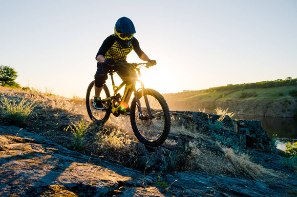 Professional Cyclist Riding the Downhill Mountain Bike on the Summer Rocky Trail at the Evening. Extreme Sport and Enduro Cycling Concept. - Foto, afbeelding