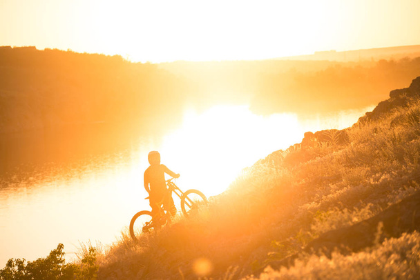 Pyöräilijä poimien hänen Mountain Bike ylös Summer Rocky Trail klo Ilta. Extreme Sport ja Enduro pyöräily käsite
. - Valokuva, kuva