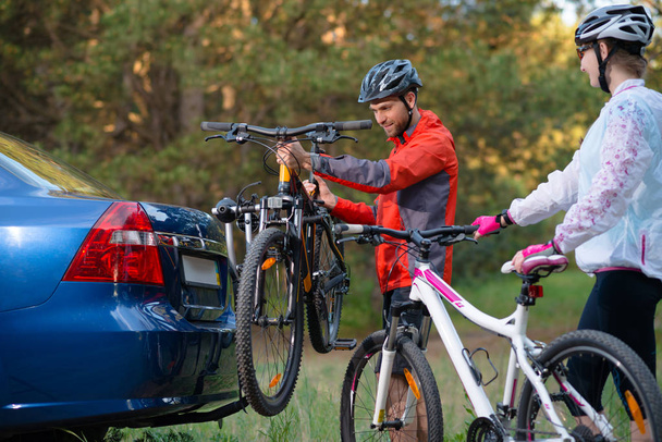 Young Couple Unmounting Mountain Bikes from Bike Rack on the Car. Adventure and Family Travel Concept. - Foto, imagen