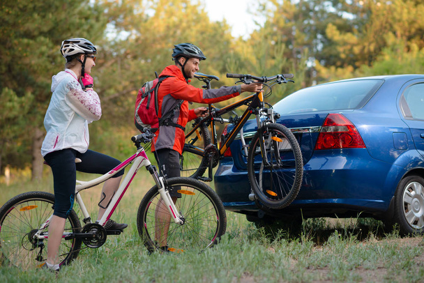 Young Couple Unmounting Mountain Bikes from Bike Rack on the Car. Adventure and Family Travel Concept. - Fotografie, Obrázek