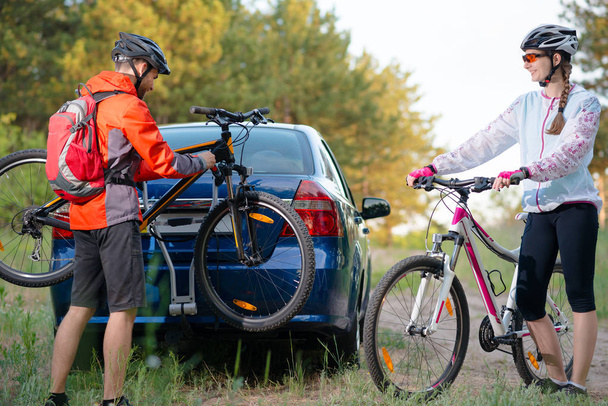 Young Couple Unmounting Mountain Bikes from Bike Rack on the Car. Adventure and Family Travel Concept. - Fotó, kép