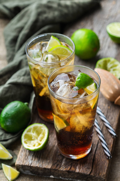 Food and drink, holidays party concept. Cuba libre or long island iced tea alcohol cocktail drink beverage, longdrink in a glass with straw, ice and lime on a dark table - 写真・画像