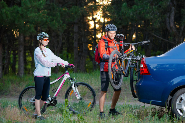 Young Couple Unmounting Mountain Bikes from Bike Rack on the Car. Adventure and Family Travel Concept. - Фото, зображення