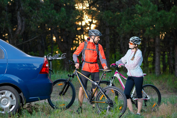 Young Couple Unmounting Mountain Bikes from Bike Rack on the Car. Adventure and Family Travel Concept. - 写真・画像
