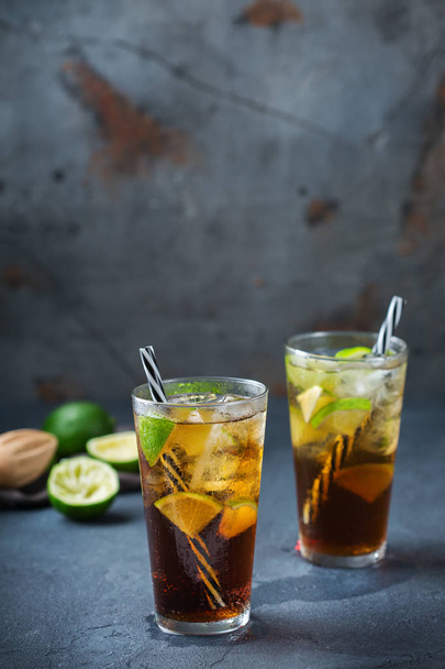 Еда и напитки, праздничные вечеринки. Кубинская либра или длинный остров ледяной чай коктейль коктейль напиток, длинный напиток в стакане с соломой, льдом и лаймом на темном столе
 - Фото, изображение
