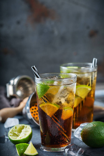 Nourriture et boissons, concept de fête de vacances. Cuba libre ou longue île thé glacé alcool cocktail boisson, longdrink dans un verre avec de la paille, de la glace et du citron vert sur une table noire
 - Photo, image