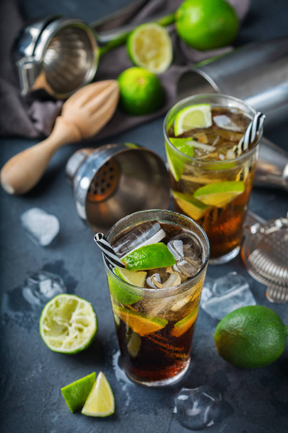 Food and drink, holidays party concept. Cuba libre or long island iced tea alcohol cocktail drink beverage, longdrink in a glass with straw, ice and lime on a dark table - Photo, Image