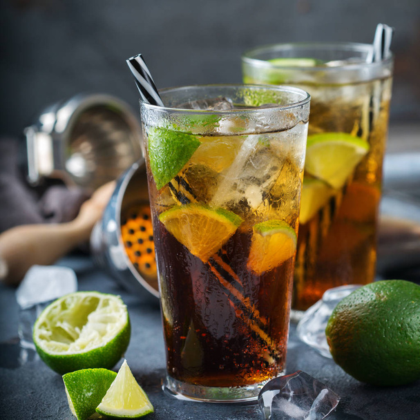 Еда и напитки, праздничные вечеринки. Кубинская либра или длинный остров ледяной чай коктейль коктейль напиток, длинный напиток в стакане с соломой, льдом и лаймом на темном столе
 - Фото, изображение