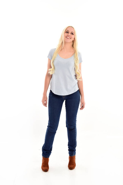 volledige lengte portret van blond meisje dragen blauw shirt en spijkerbroek, staande pose geïsoleerd op witte studio achtergrond. - Foto, afbeelding