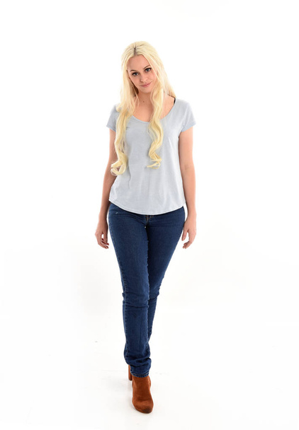 full length portrait of blonde girl wearing blue shirt and jeans, standing pose isolated on white studio background. - Фото, изображение