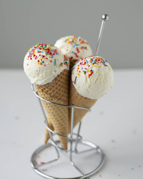 Waffle cone with white ice cream and sweet sprinkles on a light background - 写真・画像