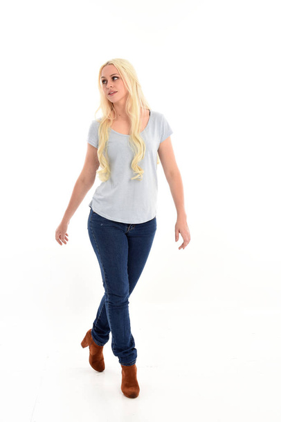 retrato de longitud completa de chica rubia con camisa azul y pantalones vaqueros, pose de pie aislado sobre fondo de estudio blanco
. - Foto, Imagen