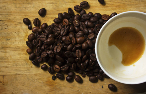 Vlekken van koffie in witte koffiemokken en koffiebonen op houten vloer. - Foto, afbeelding