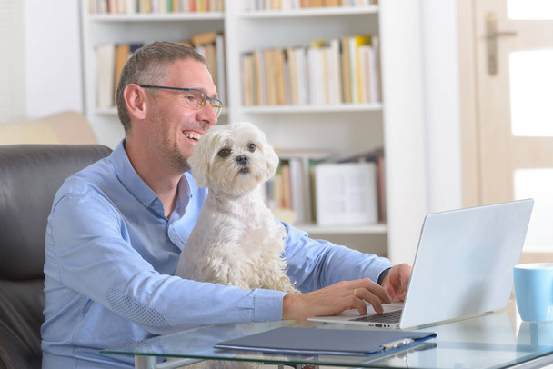 Muž pracující doma nebo v kanceláři a držící svého psa. - Fotografie, Obrázek