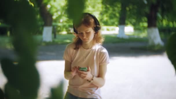 mujer patinando y escuchando música en los auriculares en el teléfono en el parque
 - Imágenes, Vídeo