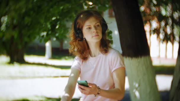 woman rollerblading and listening to music on headphones on the phone in the park - Séquence, vidéo
