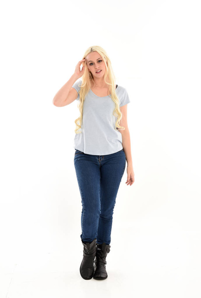 ホワイト スタジオの背景に分離されたポーズを立っている青いシャツとジーンズを身に着けているブロンドの女の子の完全な長さの肖像画. - 写真・画像