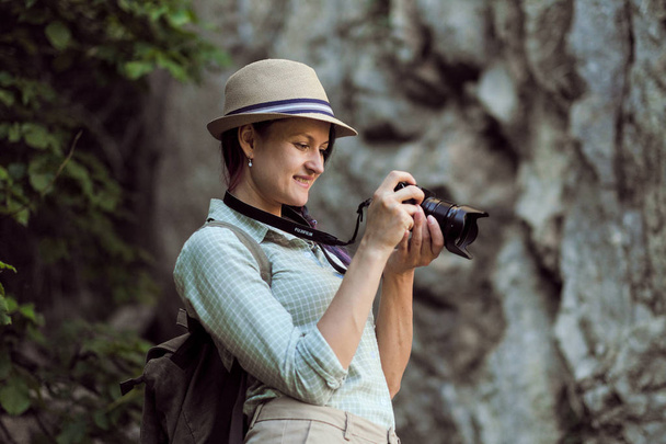 A tourist girl in a hat takes pictures of nature in the mountains. - Φωτογραφία, εικόνα