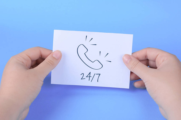 Woman's hand holding card with words "24/7" on a light blue background.  - Fotó, kép