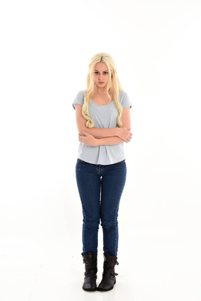 full length portrait of blonde girl wearing blue shirt and jeans, standing pose isolated on white studio background. - Photo, Image