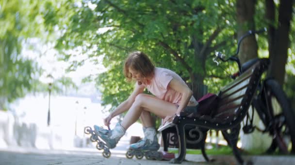 woman dresses roller skates sitting on bench in park - Imágenes, Vídeo