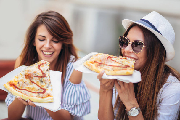 Dvě mladé ženy jíst pizzu po nakupování, baví se spolu. - Fotografie, Obrázek