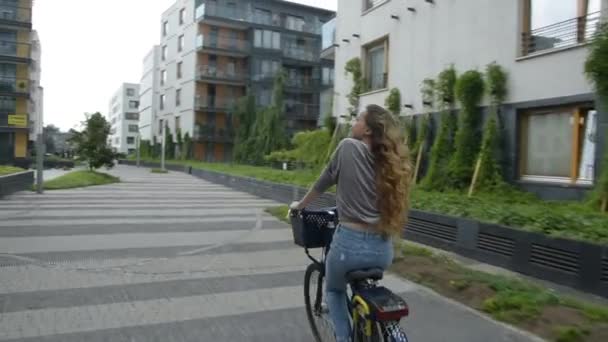 Young woman riding on bike in sunny day . Beautiful mood shot of young woman or girl riding bicycle in city. Girl with cerly hair riding on bike to her friends home, smile. 60 fps - Imágenes, Vídeo