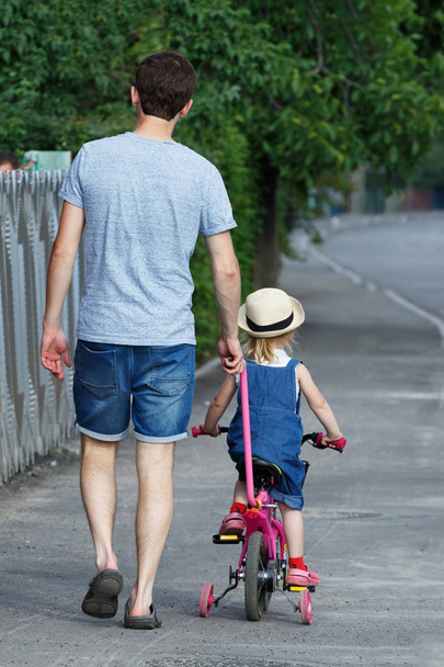 Father is teaching his daughter to ride a bicycle. - Foto, Imagem