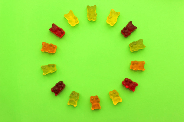 Cirkel van gummy beren in verschillende kleuren. Concept baby's. Regenboog cirkel van gekleurde snoepjes van beren op groene achtergrond, kopie ruimte.  - Foto, afbeelding