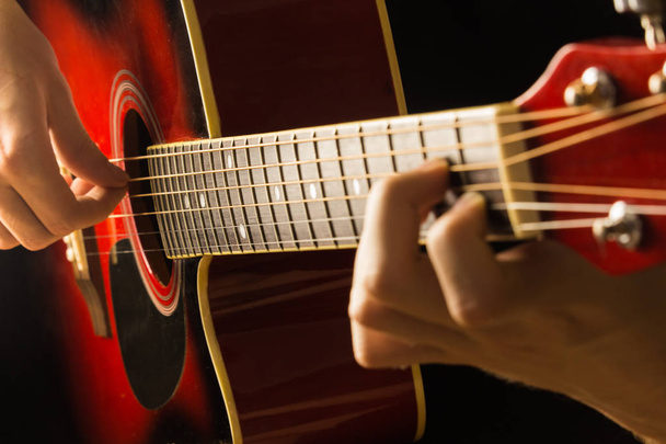 Acoustic guitar red, dark background, sits the musician playing on classical Spanish, musical school game for children and adults close-up of fingerboard and strings, the soundboard of the instrument - Foto, Imagen
