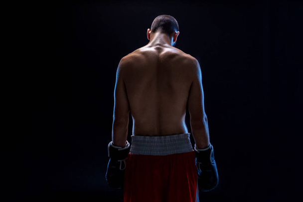 Een bokser in zijn korte broek staat met zijn rug, zijn hoofd wordt verlaagd. Recreatie. Zwarte achtergrond - Foto, afbeelding