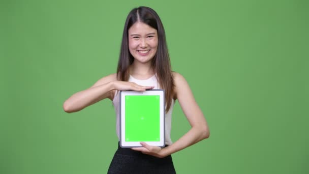 Young beautiful Asian businesswoman showing digital tablet - Felvétel, videó