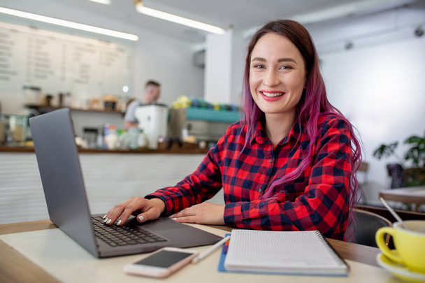 Mujer joven con el pelo rosa con ordenador portátil sentado en la cafetería, estudiante femenina inteligente que trabaja en net-book
. - Foto, Imagen