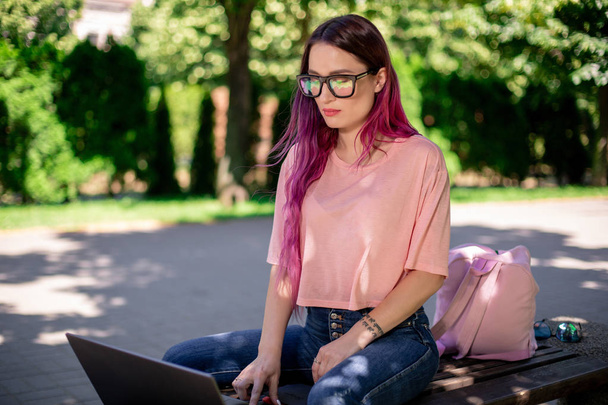 Young girl is studying in the spring park, sitting on the wooden bench and browsing on her laptop - Foto, Imagen