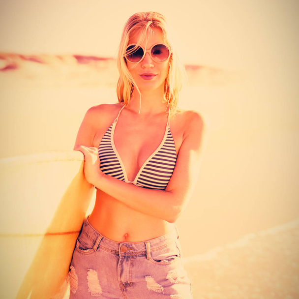 Portrait of young woman holding surfboard at beach during sunny day - 写真・画像