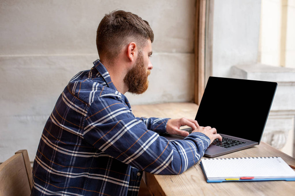 Νεαρός άνδρας συνομιλείτε μέσω net-βιβλίο κατά τη διάρκεια εργασιών σπάσει σε καφενείο, αρσενικό κάθεται μπροστά ανοικτή φορητό υπολογιστή με οθόνη κενό αντίγραφο χώρου. - Φωτογραφία, εικόνα